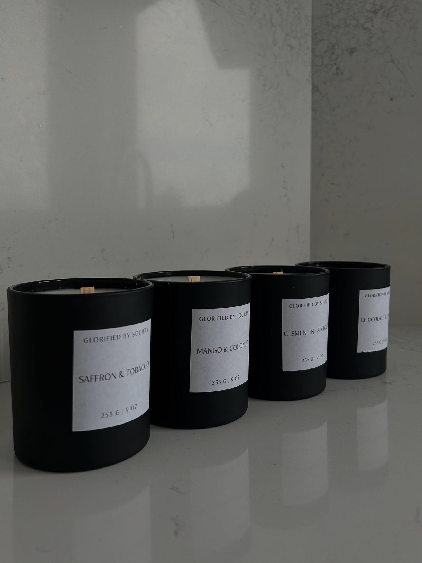 Image of a luxurious scented candle in a black matte glass jar, placed on a marble tray. The candle is made of high-quality coconut soy wax, and its wooden wick is positioned in the center of the jar. The label on the jar features a sleek and sophisticated design, with elegant, minimalist  typography. The candle emits a warm and inviting glow, creating a cozy and relaxing atmosphere in any room.